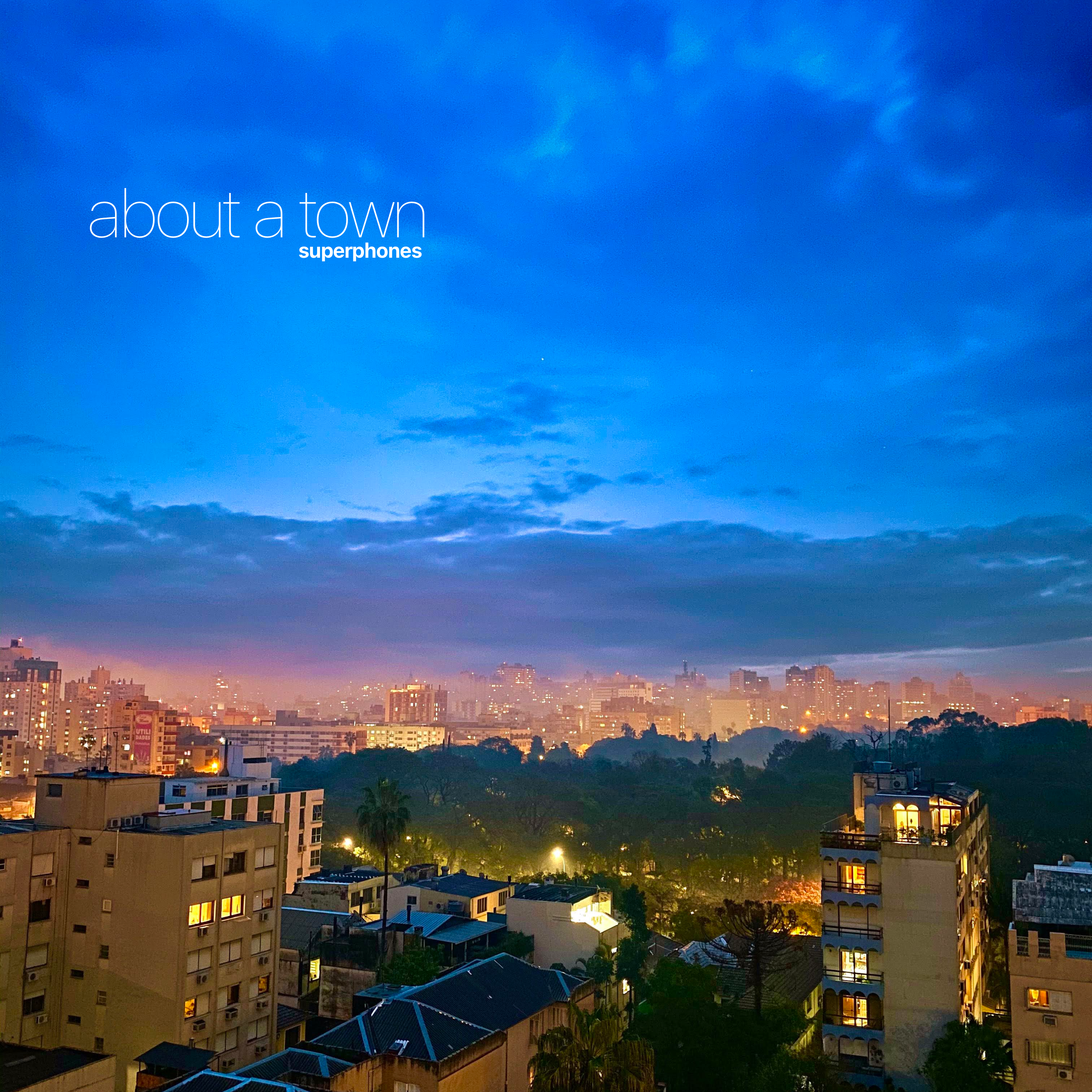 About The Town cover, with a cityscape beneath a blue sky.
