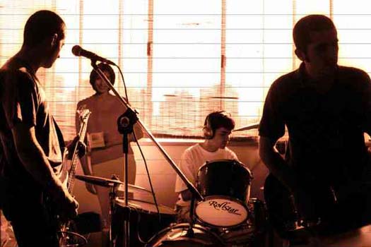 Musicians in a rehearsal room with light coming through the window.